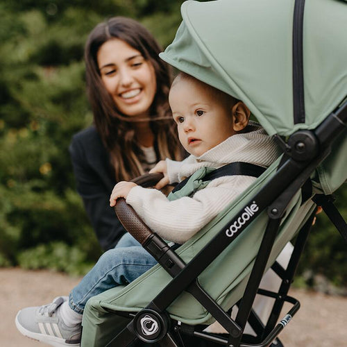 Baby im Reisebuggy, lachende Frau im Hintergrund im Park.