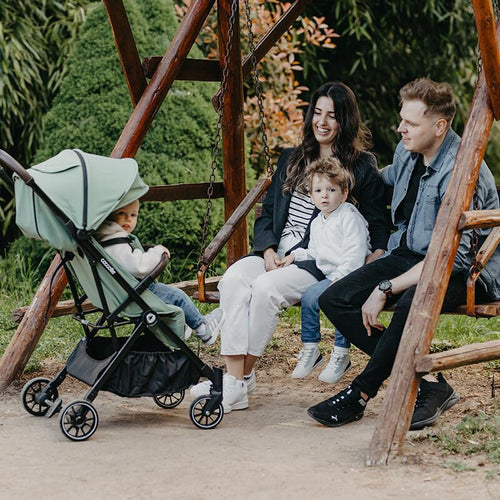 Familie auf Parkbank, Kind im Reisebuggy dabei, entspannter Tag.