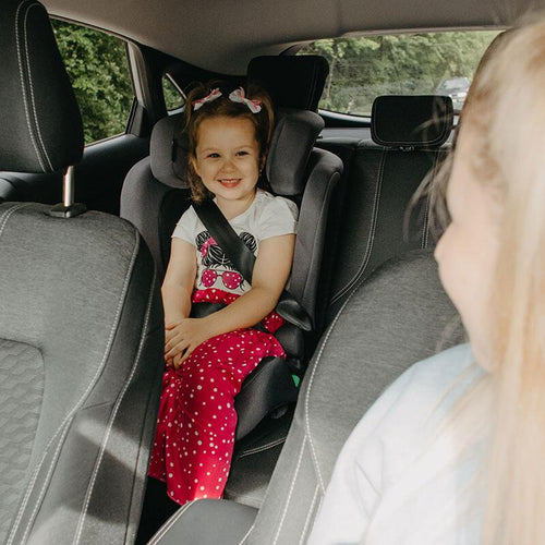 Fröhliches Mädchen sitzt sicher in einem blauen Kindersitz im Auto, schaut nach vorne.