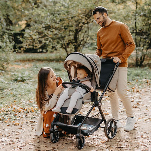  Glückliche Familie im Herbstpark; Vater schiebt Kinderwagen, Mutter kniet beim Baby.