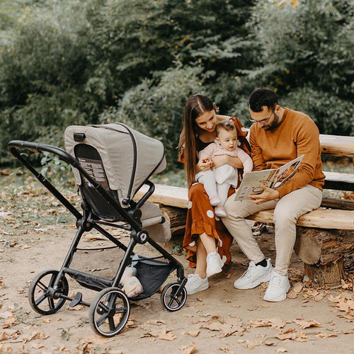 Familie sitzt zusammen auf einer Bank im Park, während das Baby im Kinderwagen schaut.