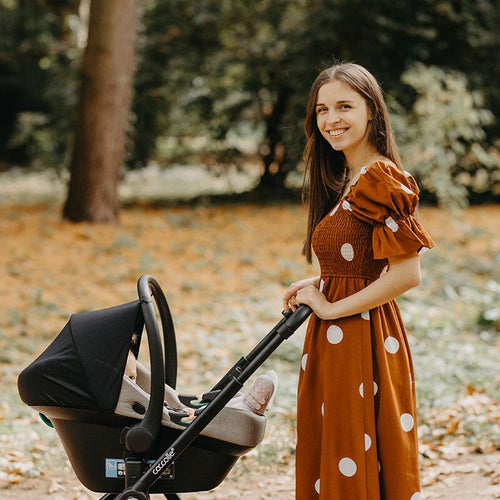 Lächelnde Mutter steht neben einem Kinderwagen im sonnigen Herbstpark.