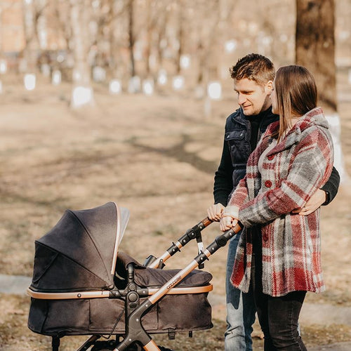 Ein glückliches Paar steht im Park und schaut auf ihren stilvollen Kinderwagen.