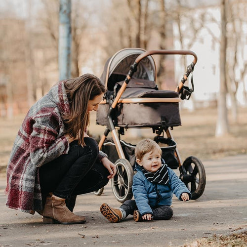 Eine Mutter sitzt auf dem Boden im Park neben ihrem Kind, das aus dem Kinderwagen ausgestiegen ist.