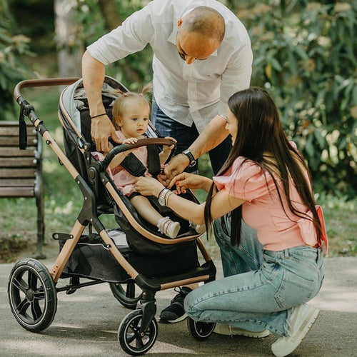 Zwei Eltern beugen sich über ihren Kinderwagen, um ihr Kleinkind im grünen Park zu sichern.