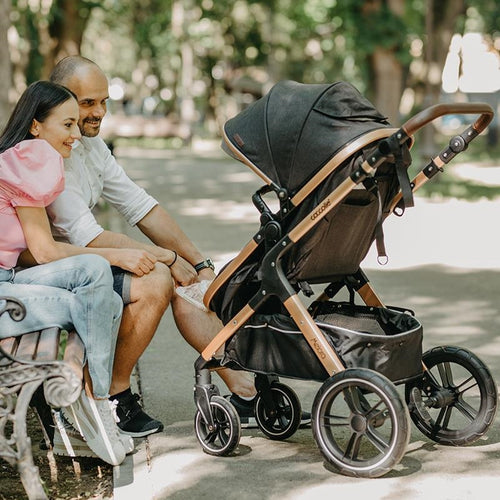 Ein junges Paar entspannt auf einer Parkbank, während ihr Kinderwagen neben ihnen steht.