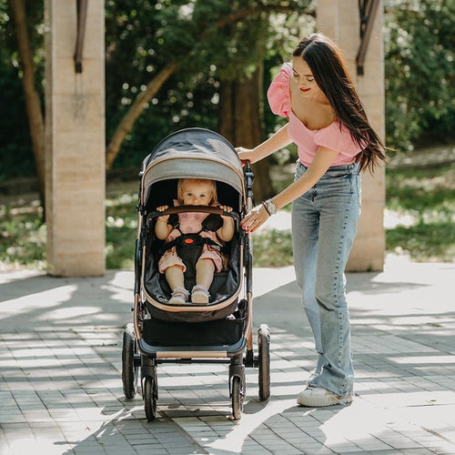 Eine Mutter lächelt, während sie ihren Kinderwagen schiebt, in dem ihr Kind sitzt und neugierig umherblickt.