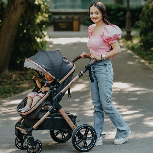 Eine junge Mutter lächelt beim Spaziergang mit ihrem Kinderwagen, in dem ein Kleinkind sitzt und nach oben schaut.