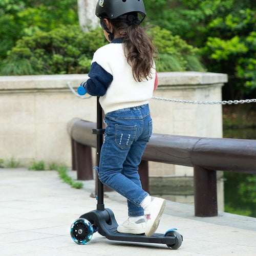 Rückansicht eines Kindes, das auf einem schwarzen Scooter mit grünen Details fährt und den Helm trägt.